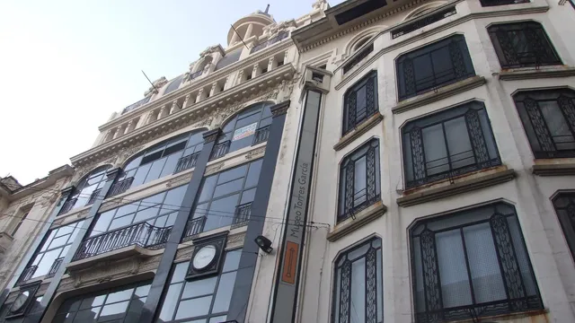 Fachada art nouveau de um prédio da rua Sarandí, em Montevidéu, vista de baixo, com grades de ferro trabalhado nas janelas e uma placa vertical do Museo Torres García.