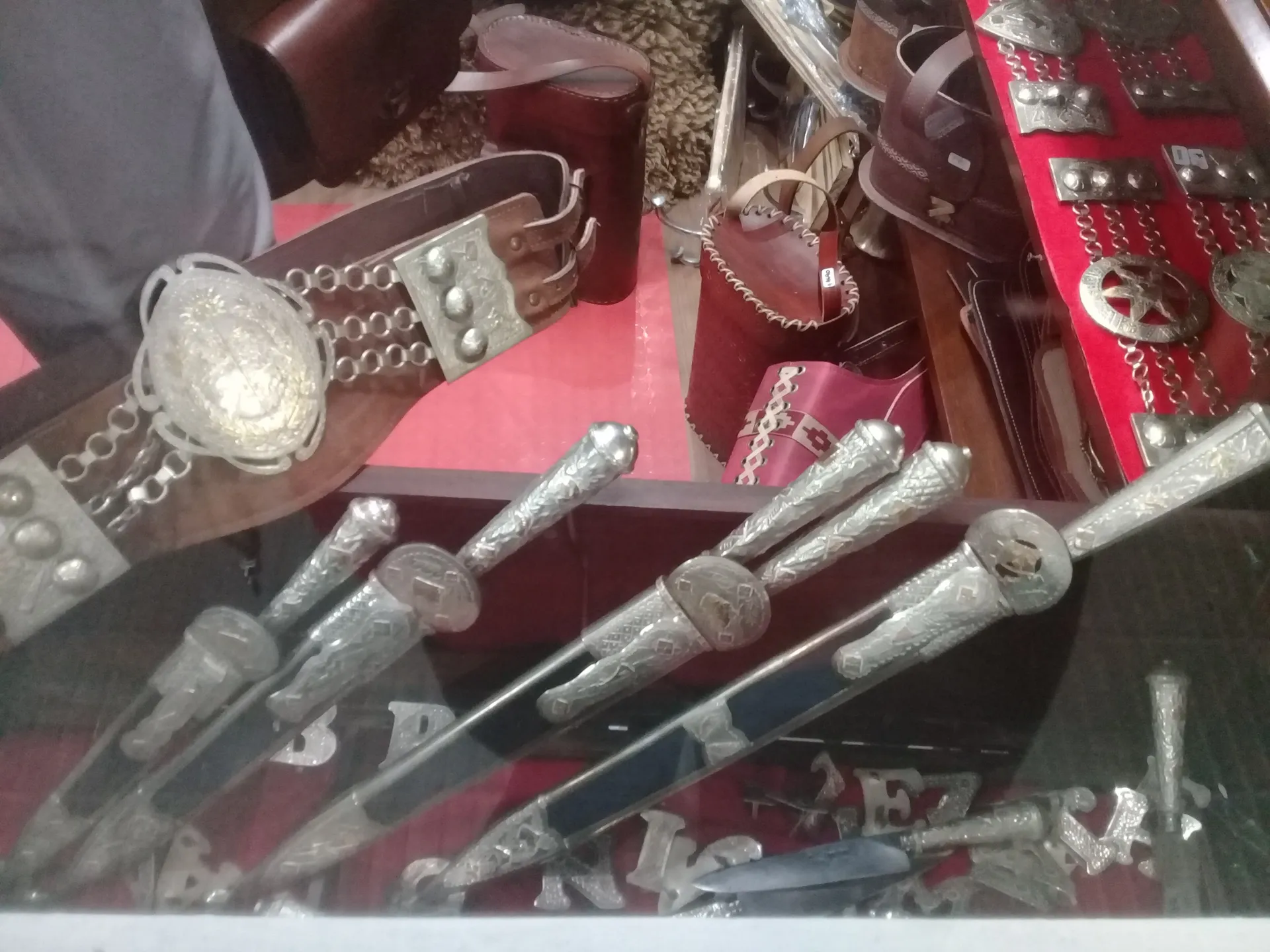Vitrine de vidro de uma talabartería uruguaia com várias facas de cabo em prata trabalhada, um tirador de couro com rastra de prata e guampas e maleteiros ao fundo