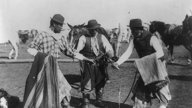 Fotografia de cerca de 1890 mostrando três gaúchos no campo, dois deles cruzando facas enquanto um terceiro usa o poncho enrolado no braço como proteção, com cavalos ao fundo.