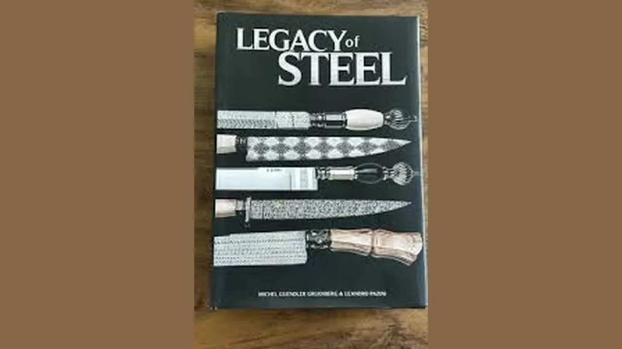 Exemplar do livro Legacy of Steel sobre uma mesa de madeira: capa preta com o título em letras prateadas e cinco facas artesanais fotografadas na vertical, com cabos de marfim, cristal e madeira e lâminas em aço damasco.