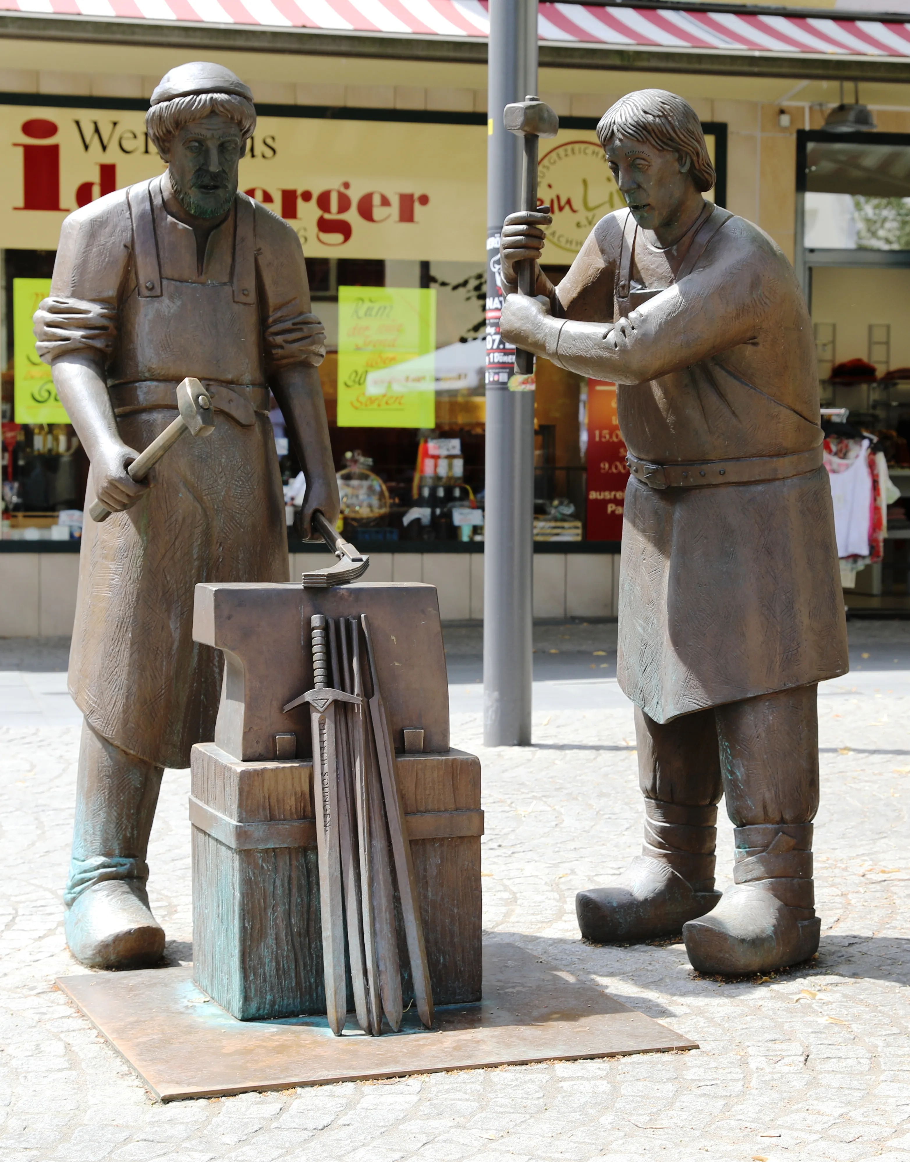 Monumento de bronze com dois ferreiros medievais trabalhando numa bigorna, cercados de espadas, uma delas com a palavra SOLINGEN gravada na lâmina